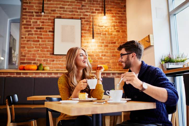 Couple of young people drinking coffee and eating cake in a stylish modern cafeteria