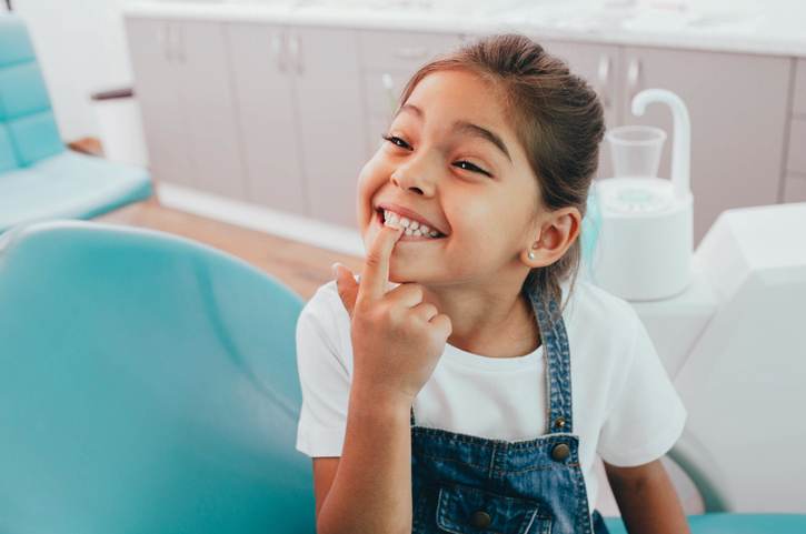 Mixed race little patient showing her perfect toothy smile while sitting dentists chair Mixed race little patient showing her perfect toothy smile while sitting dentists chair